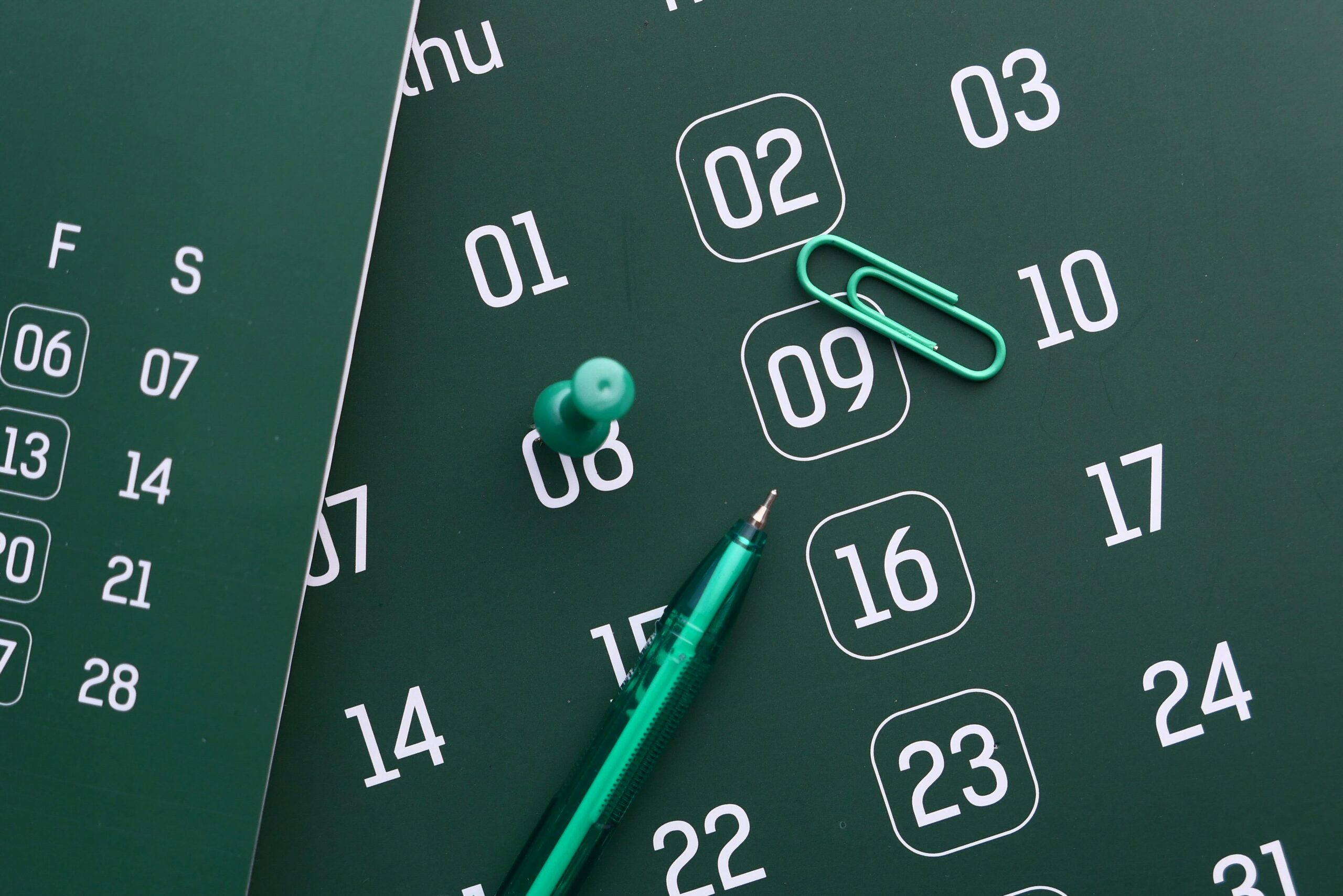 Partners Close-up of a green calendar with pen, push pin, and paper clip for planning and organization.